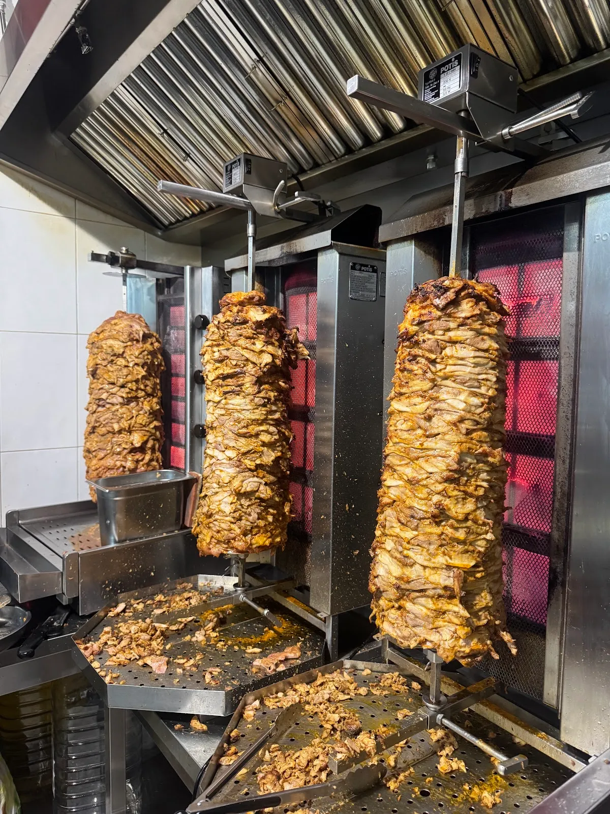 Tres asadores verticales de shawarma girando frente a las resistencias encendidas