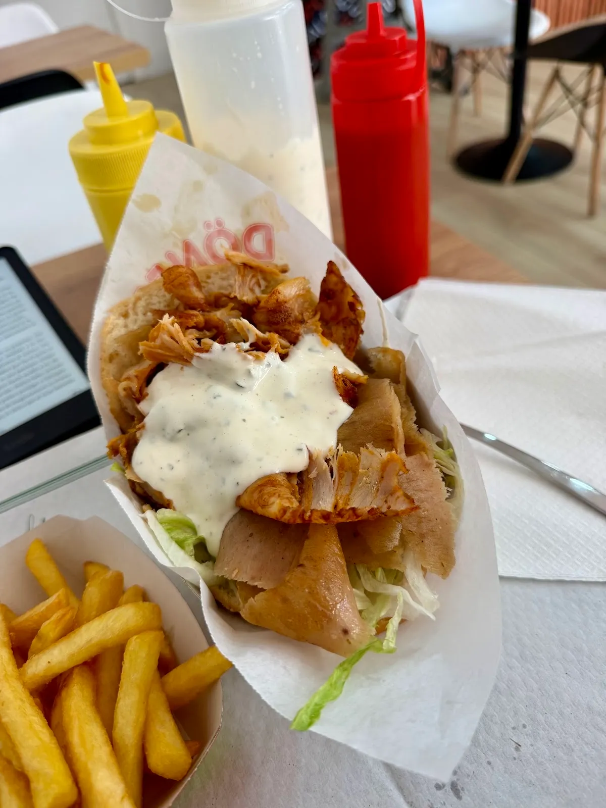 Pita de pollo en su papel, con salsa blanca de hierbas y una ración de patatas fritas