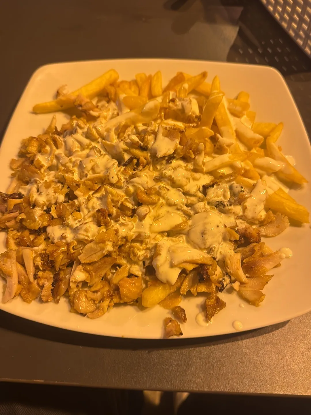Plato de shawarma de pollo con patatas fritas y salsa blanca por encima